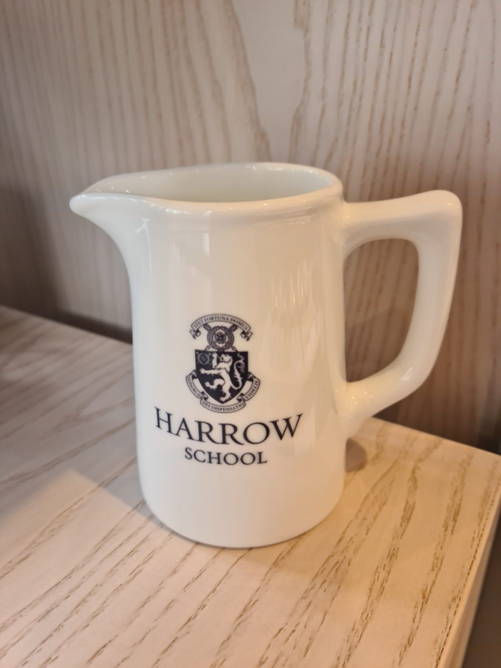 A white jug with the Harrow School crest on